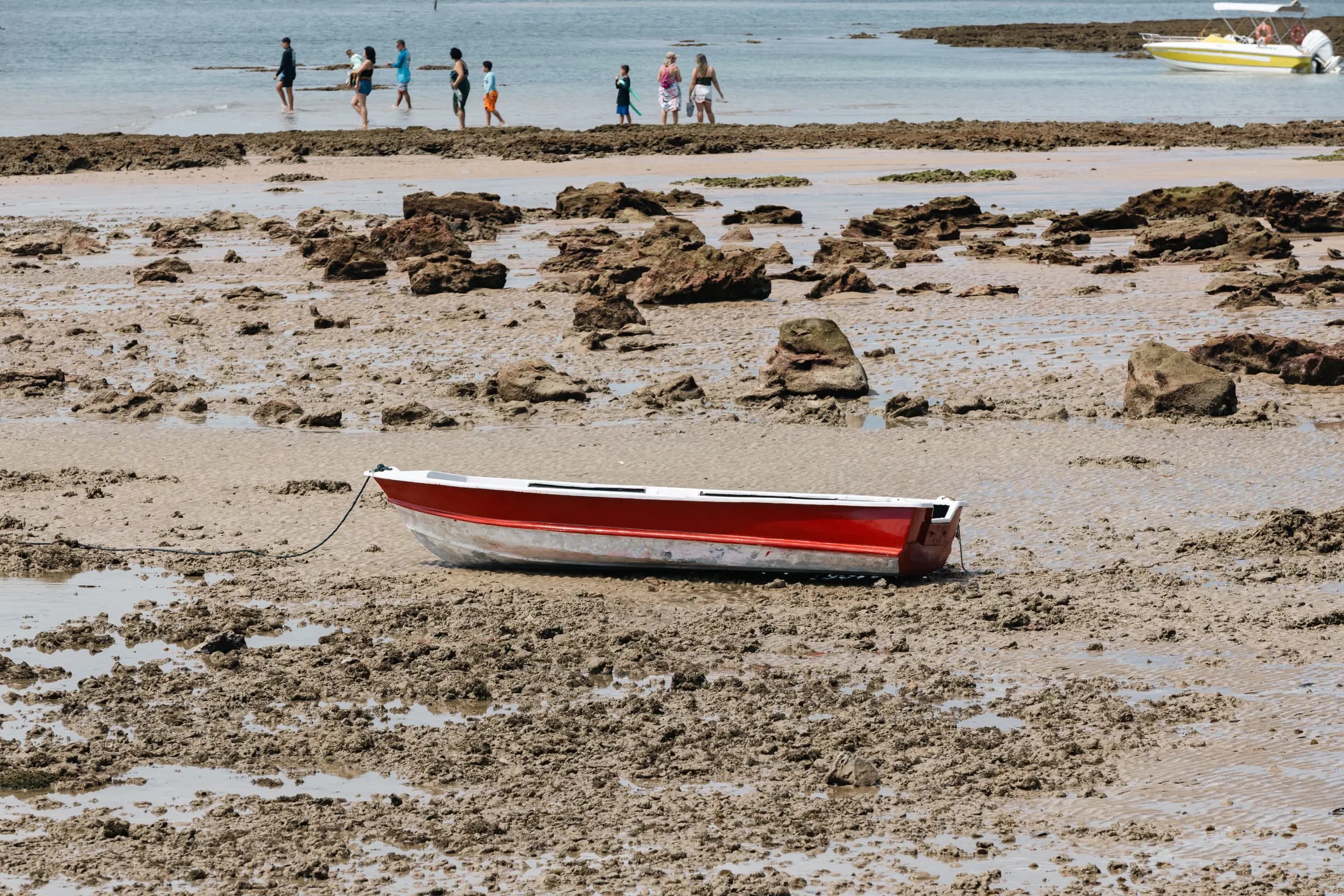 Barco vermelho encalhado na maré baixa, entre poças e pedras