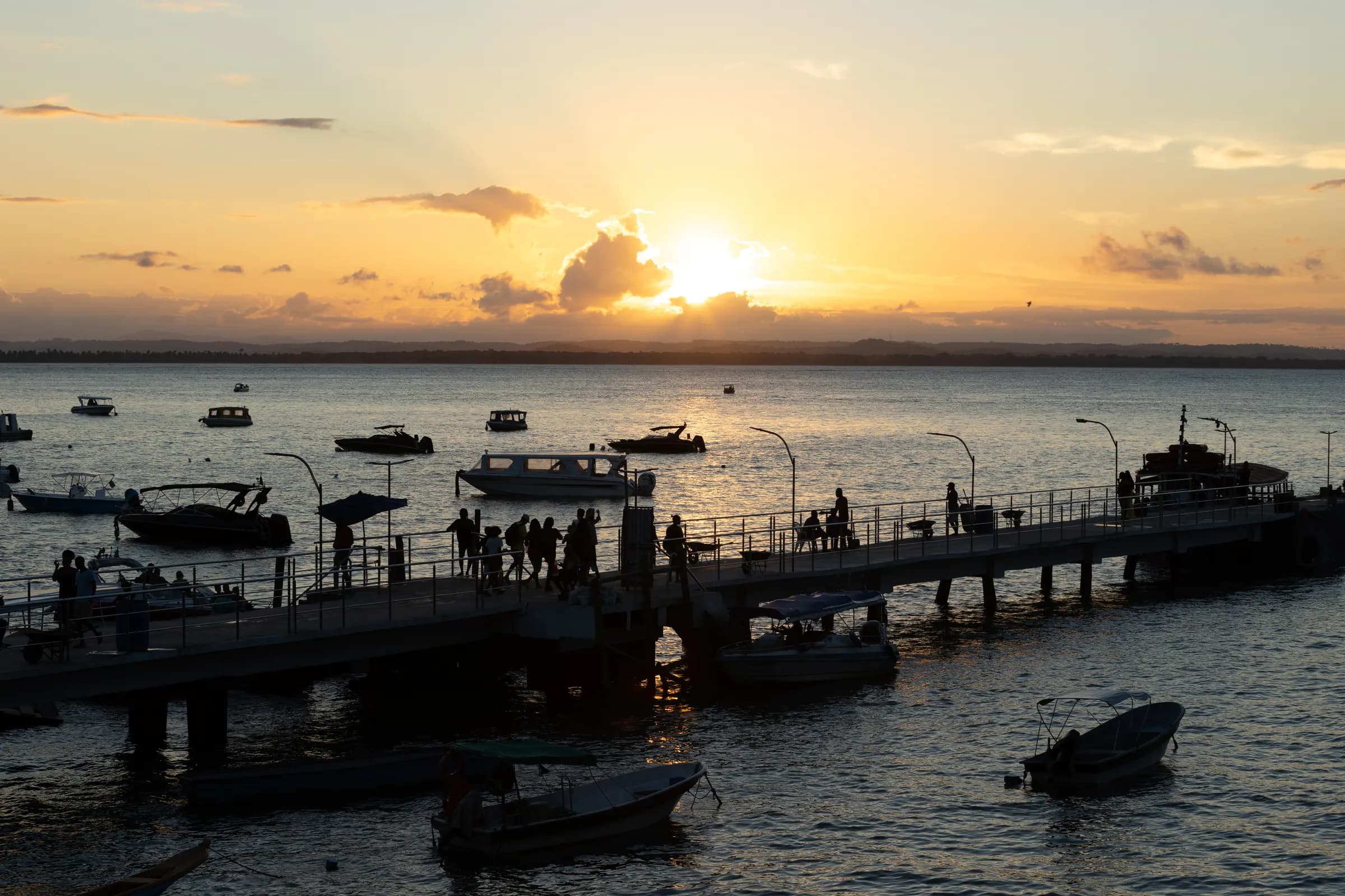 Pôr do sol sobre o mar, com barcos e o cais de Morro de São Paulo em silhueta
