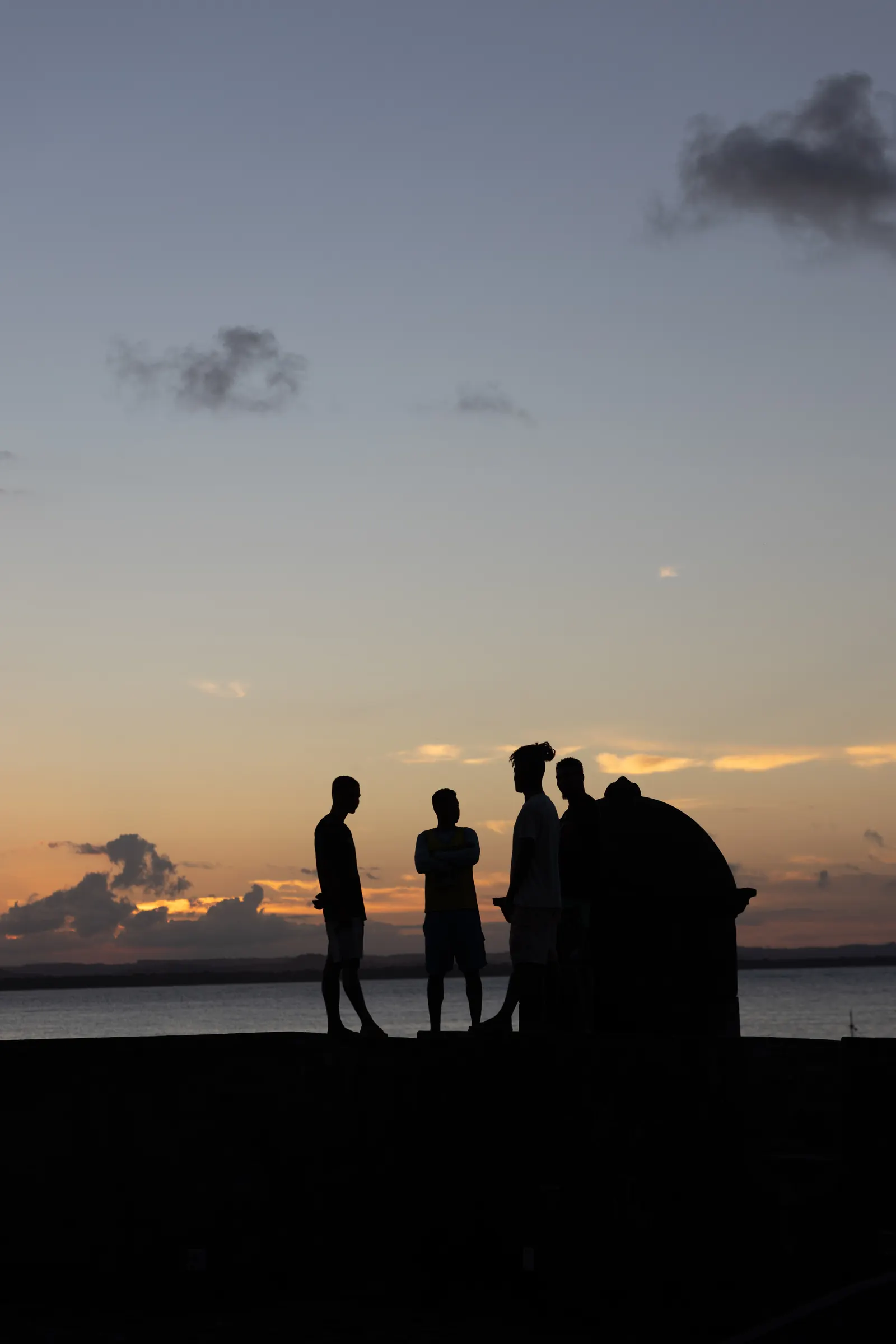 Silhuetas de pessoas contemplando o céu alaranjado ao pôr do sol